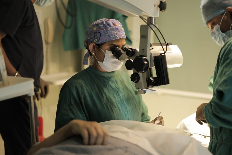 Dr. Anchal Gupta in green theatre scrubs at the operating microscope